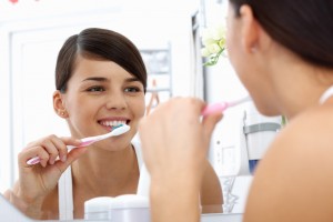 Young pretty woman brushing teeth in front of the mirror